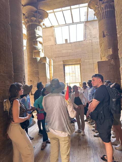       A group of tourists inside an ancient temple with a guide.
  