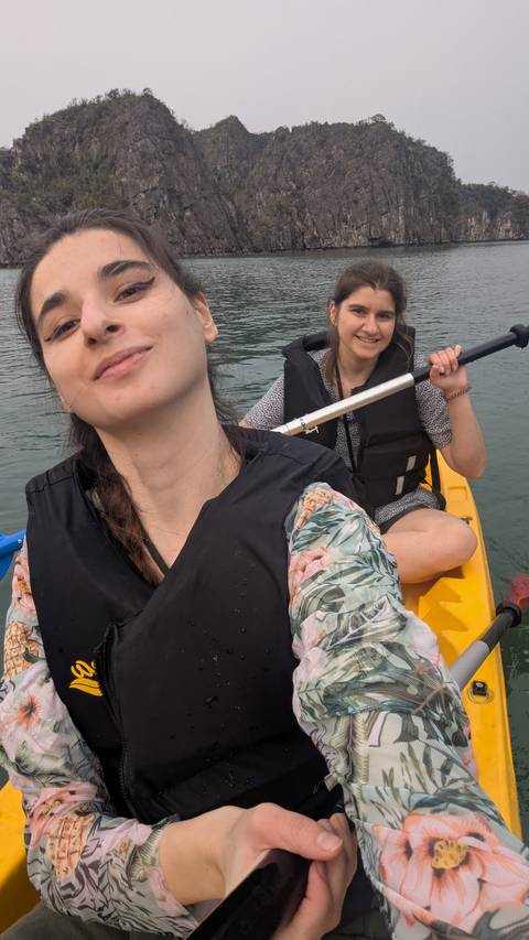       Two women kayaking on a calm body of water.
  