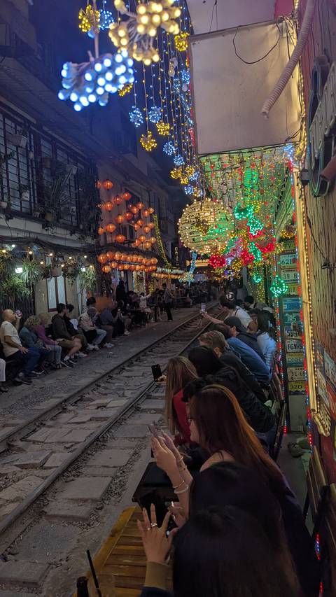       A bustling narrow street with colorful lights and people dining.
  