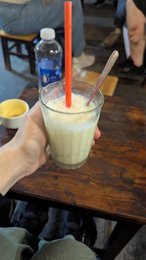       A hand holding a glass of milkshake with a straw.
  