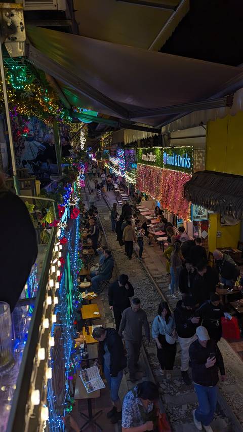       A lively street with colorful lights and people dining along railway tracks.
  