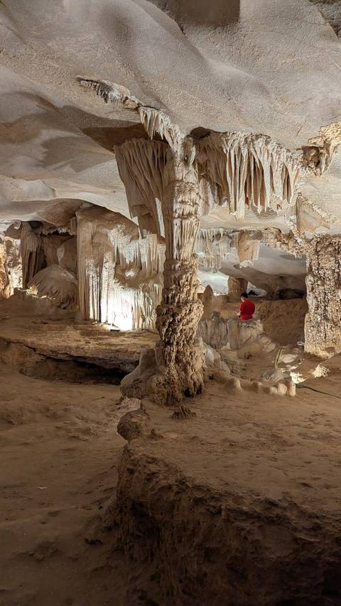       Person exploring a cave with stalagmites and stalactites.
  