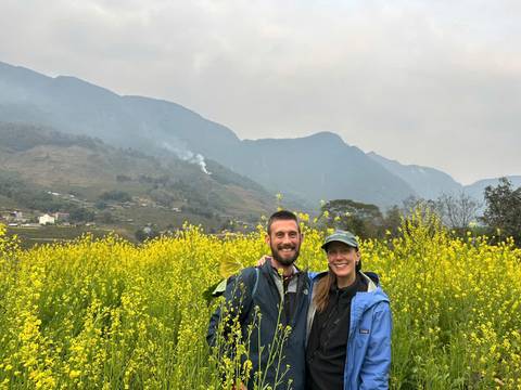 Couple smiling in a field of yellow flowers with mountains