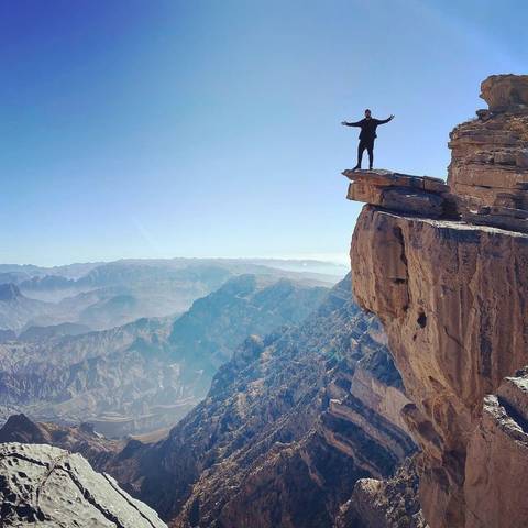 Person standing on a cliff overlooking a vast mountain landscape.