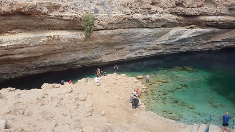 People exploring a large natural sinkhole with clear water.