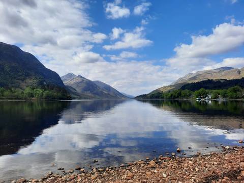 Reflective lake surrounded by mountains under a blue sky.