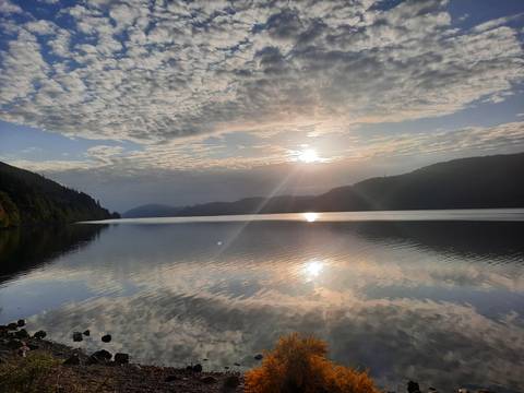 Sunset over a calm lake with clouds reflecting in the water.
