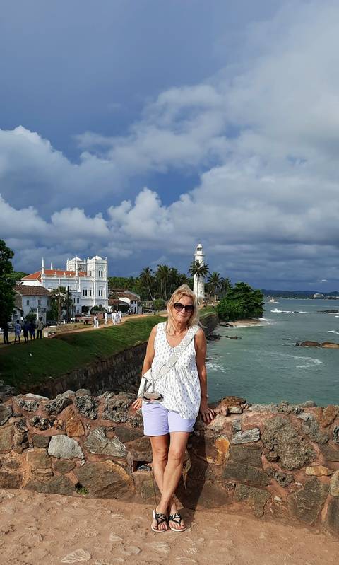 Woman standing by the ocean with a lighthouse in the background.