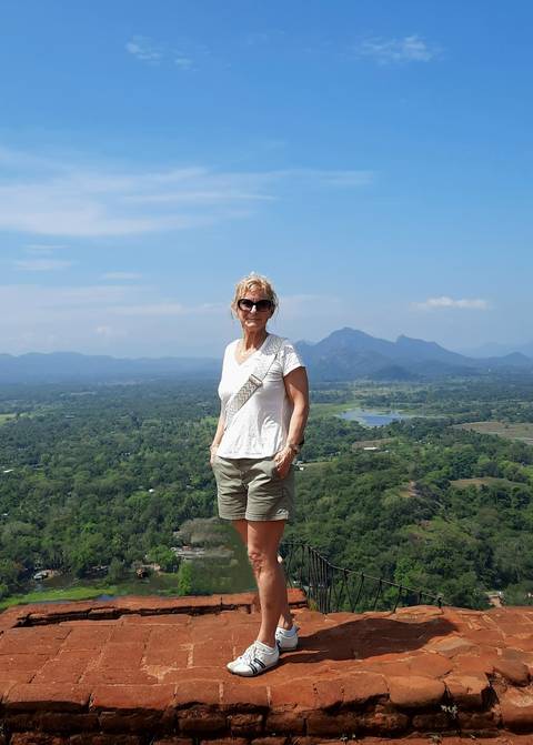 A person posing with scenic mountains and greenery in the background.