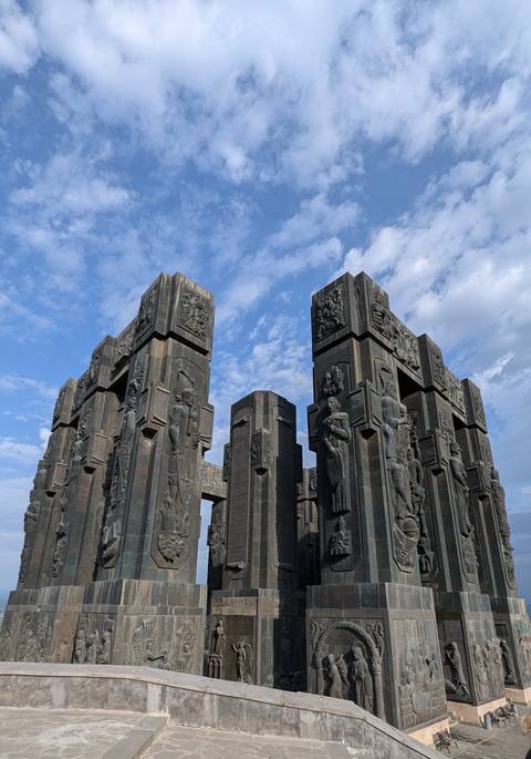       Monument with tall sculpted pillars against a blue sky.
  