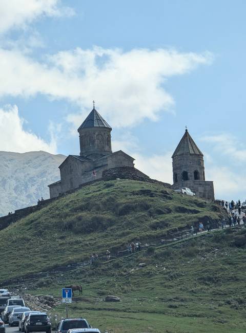       Historical church with two bell towers on a hill against a mountainous backdrop.
  