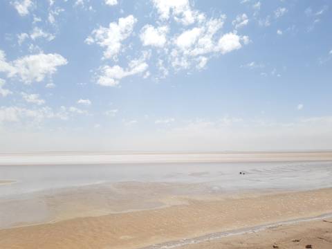 A vast, flat salt landscape under a bright blue sky with scattered clouds.