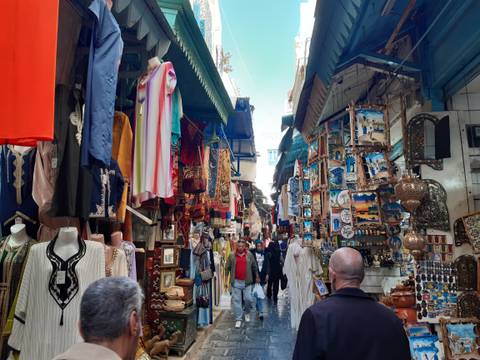 Bustling market street with colorful textiles and crafts under a blue sky.