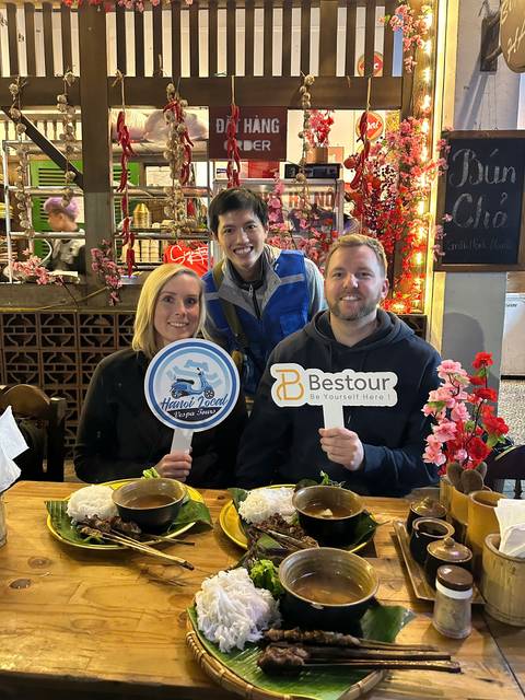 Three people posing with 'Hanoi Local' and 'Besttour' signs at a restaurant.