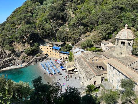      Aerial view of a secluded beach with historic buildings and clear water.
  