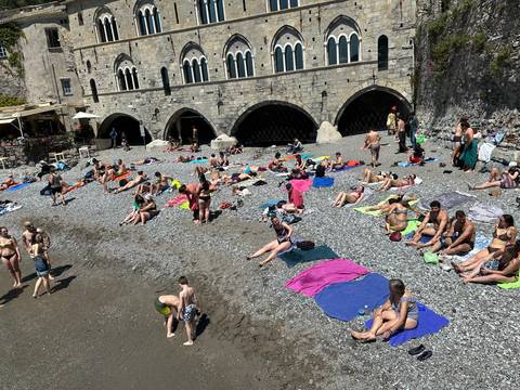 People relaxing on a pebble beach in front of a historic structure.