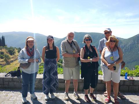 Tourists posing with a scenic Greek landscape in the background.