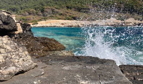       Waves crashing on rocks by the shore with clear blue water.
  