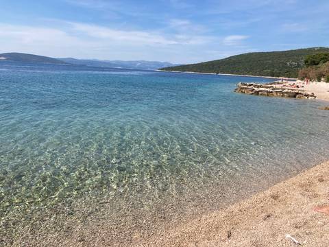       Clear pebbled beach facing a calm blue sea.
  