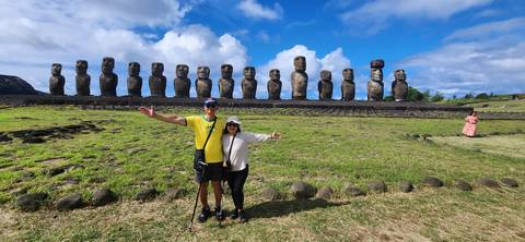 Couple posing in front of Moai statues on a grassy field.