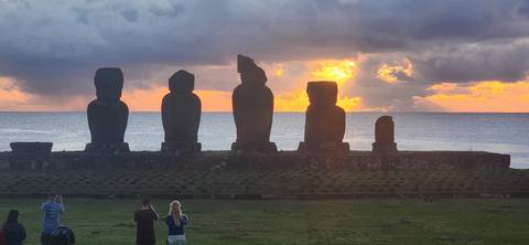 Silhouettes of Moai statues at sunset with ocean view.