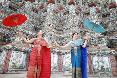 Two women in traditional dress with umbrellas in front of decorative temple.