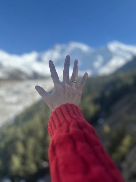       A hand with a ring reaching towards snow-capped mountains.
  