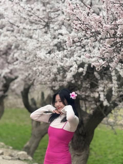       Woman in pink smiling with cherry blossoms in the background.
  