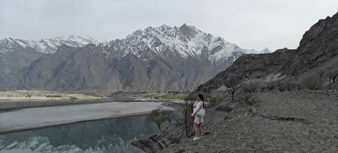       A woman standing by a lake with mountains in the background.
  