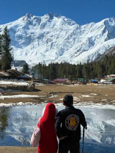       Two people on a snowy landscape with cabins and trees.
  