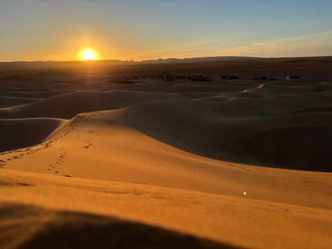       Sunset over sand dunes with scattered huts in the distance.
  