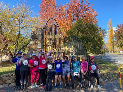       Group of cyclists posing under a 'Welcome to Beautiful Bright' sign.
  