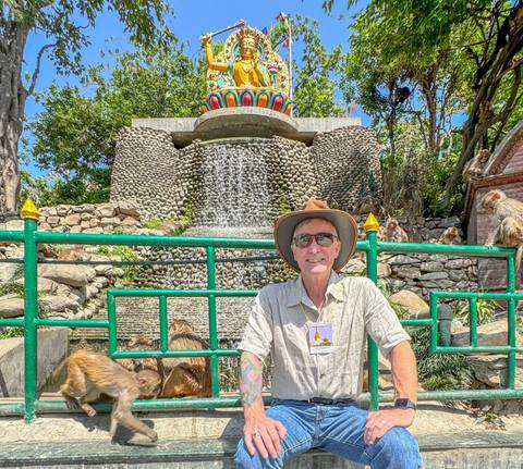Tourist posing near a fountain with monkeys nearby.