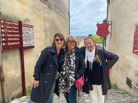 Three women posing in a quaint street with signage.