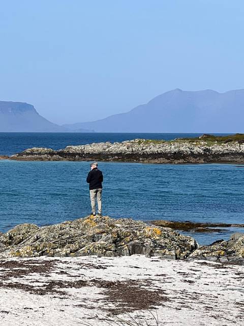       Person standing by the sea with a backdrop of distant islands.
  