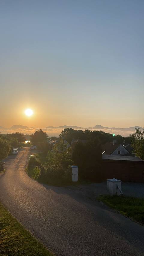       Sun setting over a town with mist and mountains in the background.
  