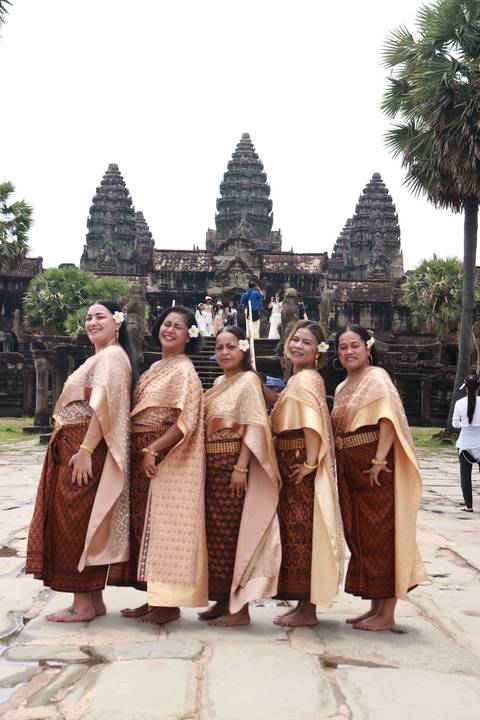       Group of women in traditional clothing posing in front of an ancient temple.
  