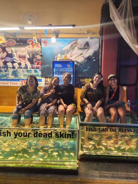 Women sitting with their feet in water, enjoying a fish spa.