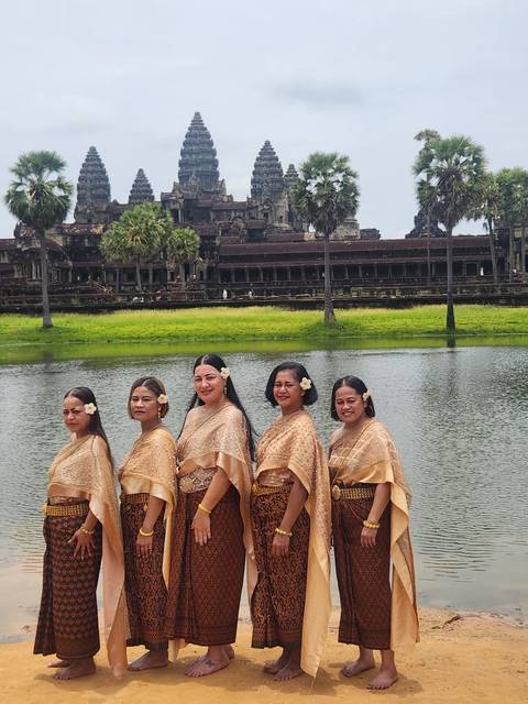 Women in traditional attire posing by a temple with a pond.