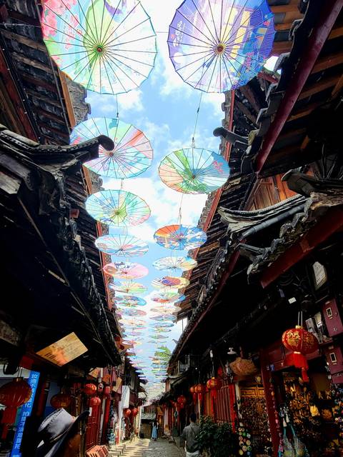Artistic umbrellas hanging in a narrow alleyway between traditional Chinese rooftops.