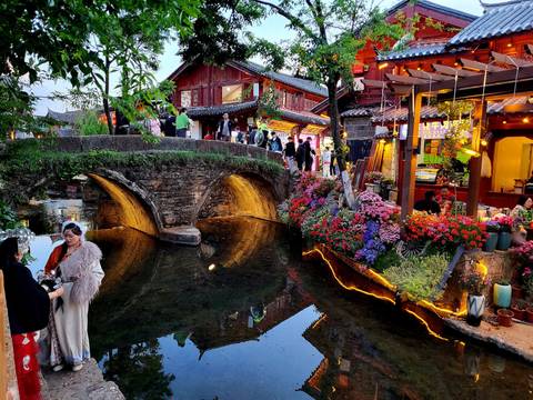       Scenic view of a traditional bridge over a stream with flowers and people.
  