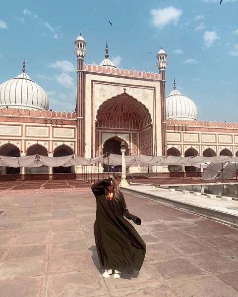 A person standing in front of a large mosque with domes.