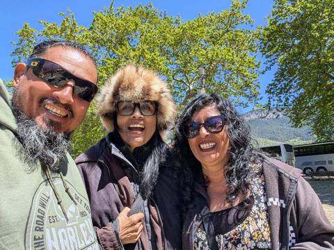       Three people smiling outdoors with greenery in the background.
  