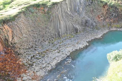 Hexagonal basalt columns by a turquoise pool.