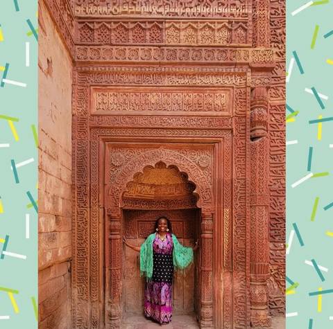       Ornate red sandstone archway with person standing.
  