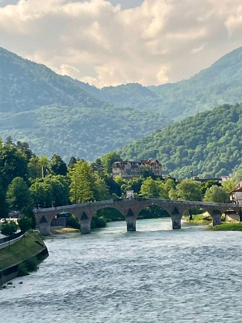 Stone bridge over a river with lush green surroundings and a building.