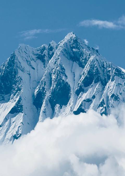       Close-up of a snowy mountain peak with blue sky and clouds.
  