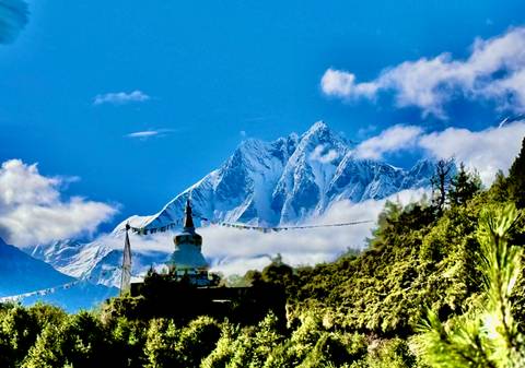       Snow-capped mountains with a stupa and prayer flags in the foreground.
  