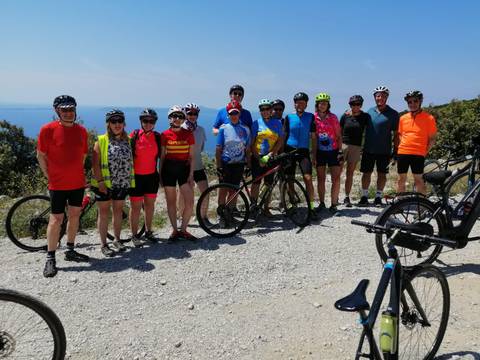       A group of cyclists posing for a photo on a gravel path with a scenic view.
  