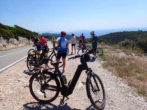       Cyclists gathered on a rural road with mountainous scenery.
  